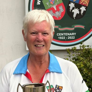 Older woman holding a trophy with a centenary sign behind her.