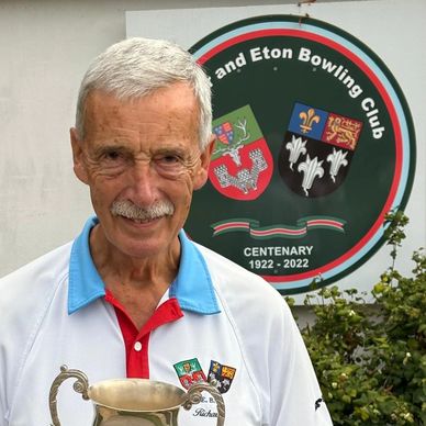 Elderly man holding a trophy at a bowling club.
