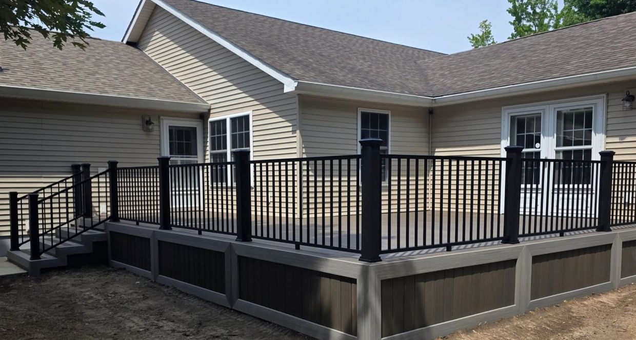 Modern elevated deck with black railings attached to a beige house.