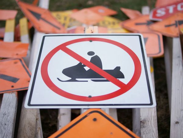 No snowmobiling allowed sign with multiple road signs in the background.