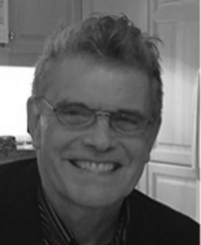 Black and white photo of smiling Caucasian man with short hair and glasses.