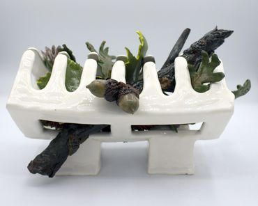 ceramic sculpture of white claw clip filled with leaves and twigs