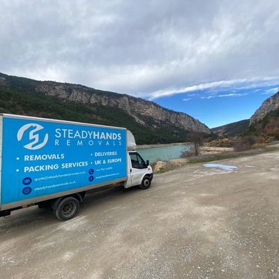 A removals van parked by a lake in Europe.