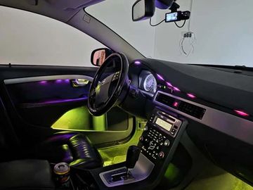 Car interior illuminated with vibrant purple and green ambient lights, showcasing a modern dashboard and leather seats.