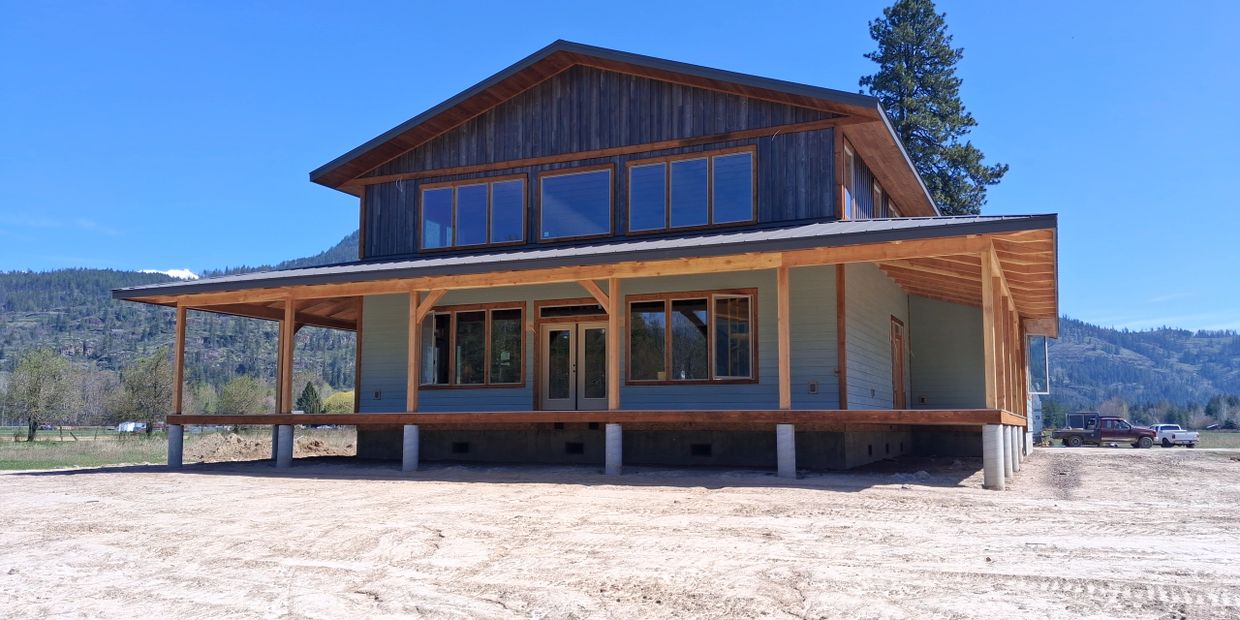 A newly constructed wooden house with a large porch in a rural setting.