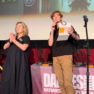 Two people on stage with microphone and awards.