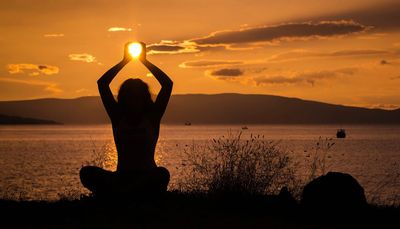 Femme devant un coucher de soleil et un lac qui entoure de ses mains la lumière du soleil 