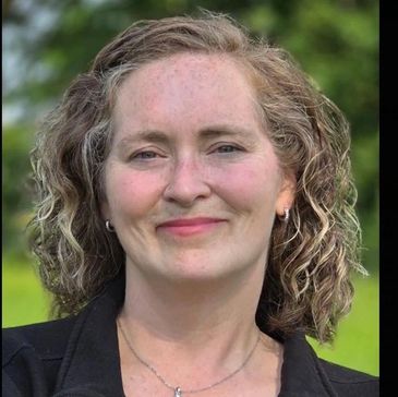 Smiling woman with curly hair outdoors.