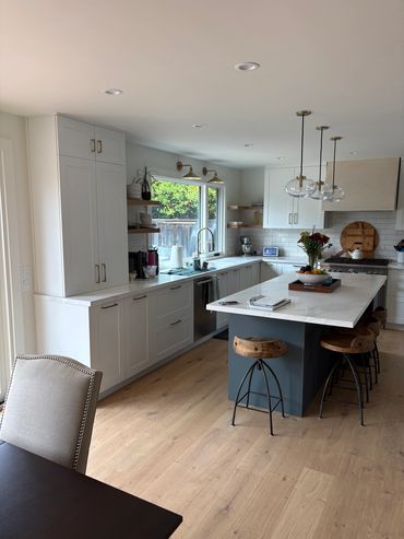 Bright kitchen with white cabinets, wooden stools, and a large island.