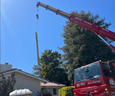 Red crane lifting a long wooden beam over a house on a sunny day.