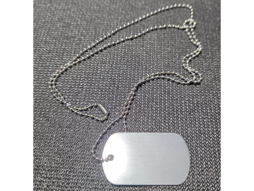 Silver dog tag with beaded chain on textured black surface.