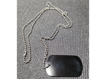 Close-up of a metallic dog tag on a beaded chain against a textured fabric background.
