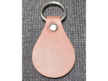 Brown leather keychain with a metal ring on a textured black surface.