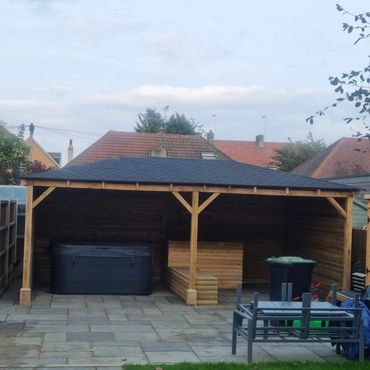 A bespoke oak pergola with a pitched roof enclosing a hot tub and bar area in a back garden.