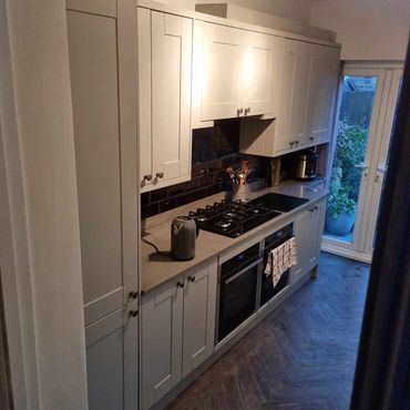 A grey kitchen with a grey worktop, antique brass handles and herringbone laid flooring.