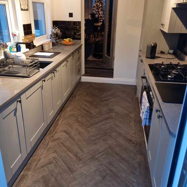 A grey kitchen fitted with a grey worktop and antique brass handles with black appliances.