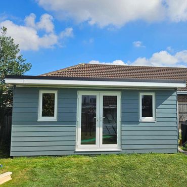 A blue cladded summer house with flat roof in a back garden.