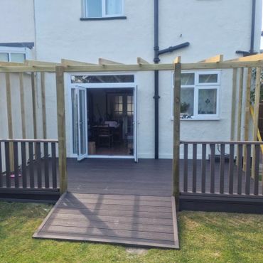 A wooden pergola, surrounded by brown composite decking in a back garden.