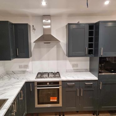 A white marble effect laminated worktop on a navy blue kitchen with satin appliances and handles.