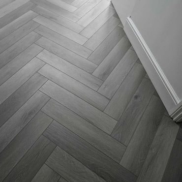Grey vinyl click laminate flooring laid in a herringbone pattern.