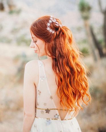 Woman with long red hair adorned with white flowers.