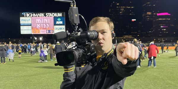 Person filming at a stadium at night, pointing at the camera.