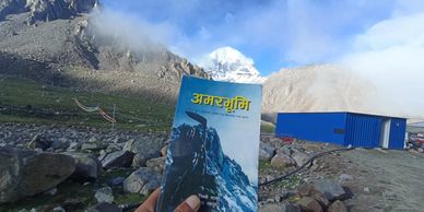 A person holds a book titled 'अमरभूमि' at Mount Kailash.