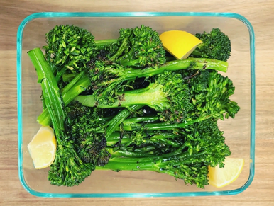 Bright green grilled broccolini with fresh lemon quarters in glass containers ready for delivery 