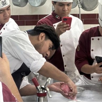 Chefs in training capturing a pastry-making demonstration on their phones.