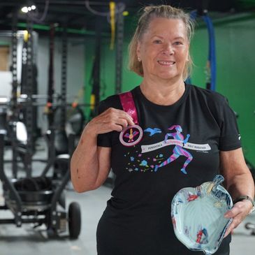 Older woman proudly holding a medal and paddle in a gym.
