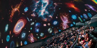 Audience watching a colorful cosmic show in a planetarium dome.