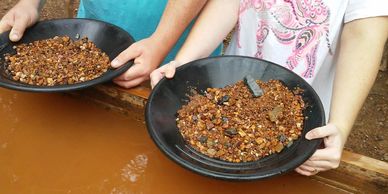 Two people holding pans with gravel and rocks, panning for gold.
