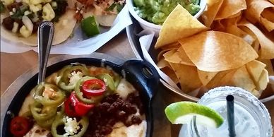 A Mexican meal with tacos, chips and guacamole, melted cheese with jalapeños, and a margarita.