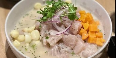 A bowl of creamy ceviche with corn, sweet potatoes, and red onion garnish.