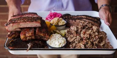 A platter of smoked meats and sides on a white tray.