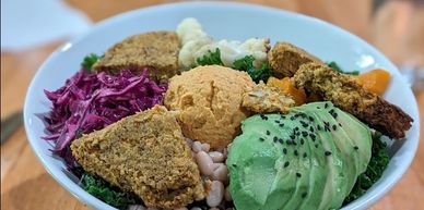 A vibrant bowl with avocado, chickpea hummus, falafel, beans, and colorful veggies.