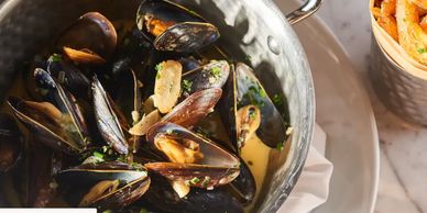 A pot of cooked mussels with garlic and herbs, accompanied by a side of seasoned fries.