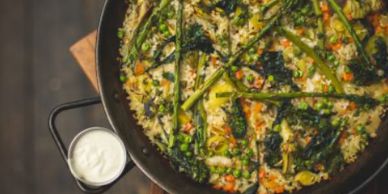 Vegetable paella with asparagus and peas served with a side of white sauce.