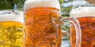 Three large glass mugs filled with beer on a sunny day outdoors.