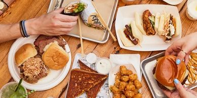 A diverse spread of casual foods including burgers, pizza, and sushi on a wooden table.