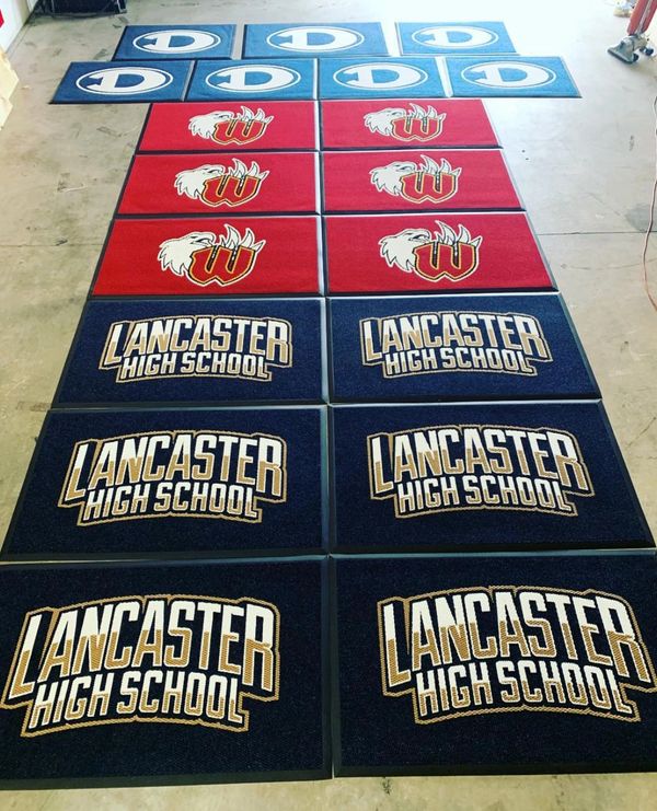 Rows of colorful school mats with logos and names on a floor.