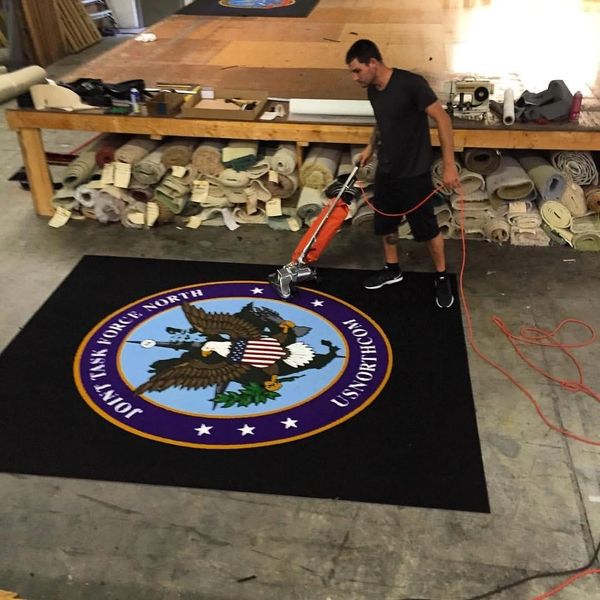 A man cleans a black rug with a military emblem in a workshop.