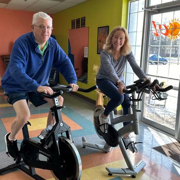 Two clients on stationary bikes at SOL Fitness studio in Janesville, WI during a workout.