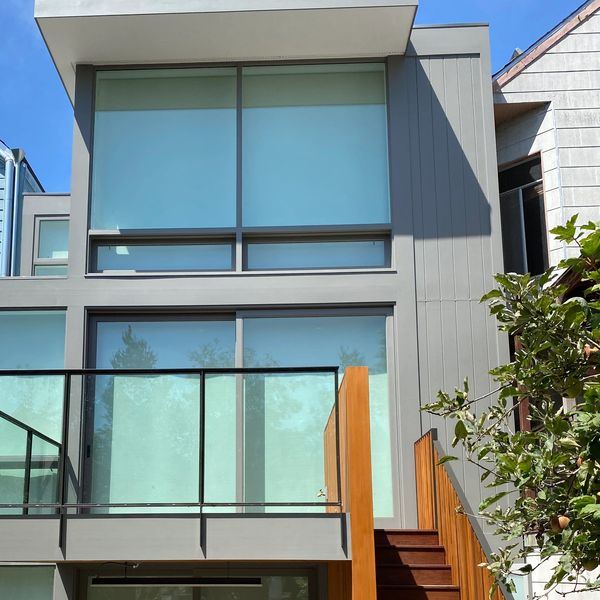 Modern gray house with large windows and wooden staircase under a clear blue sky.