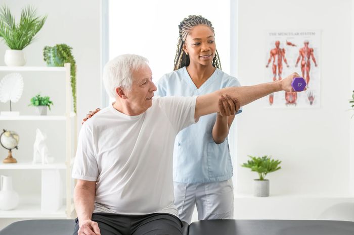 Therapist assisting elderly man with arm exercises using a dumbbell.