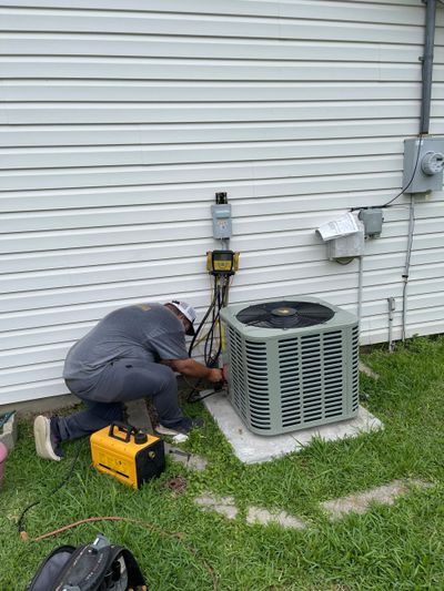 Technician working on an outdoor air conditioning unit beside a house.