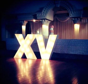 Illuminated XV letters glowing on a polished wooden floor in a dimly lit room.