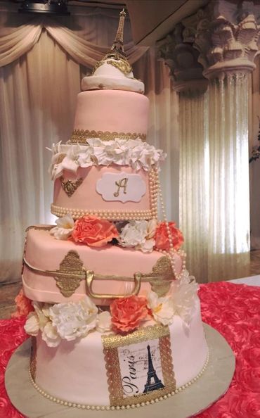 Elegant pink and gold Paris-themed tiered cake with Eiffel Tower topper and floral decorations.