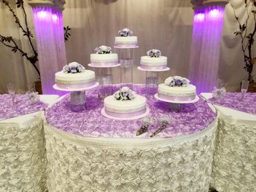 Elegant multi-tiered white cakes with purple floral decorations on a purple rose-patterned table.