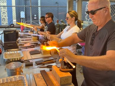 People shaping glowing glass rods in a workshop setting.